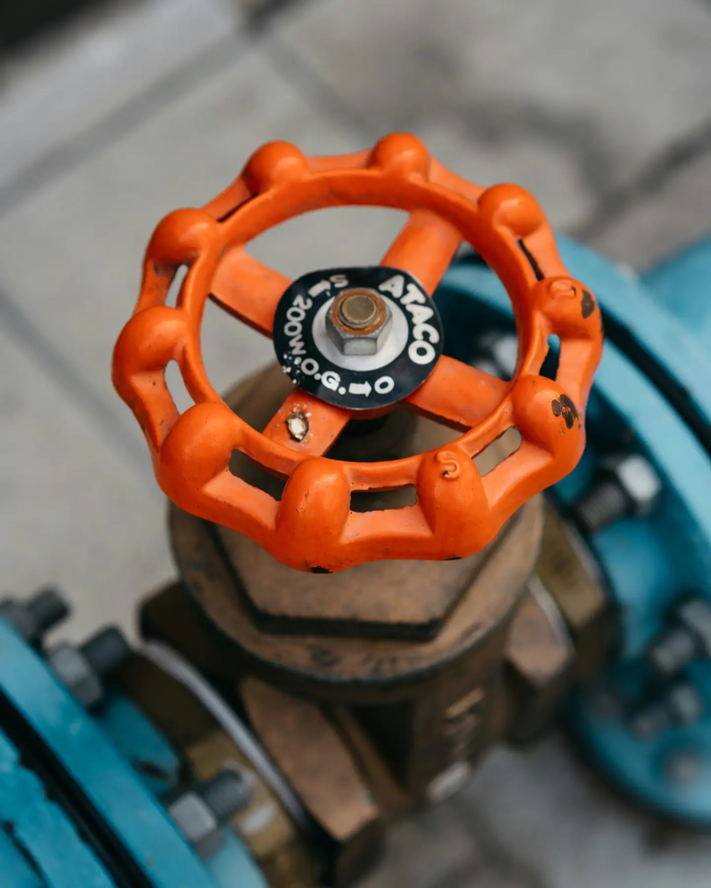 Close-up of an orange handwheel shut-off valve on a brass water main, with painted blue pipework behind it
